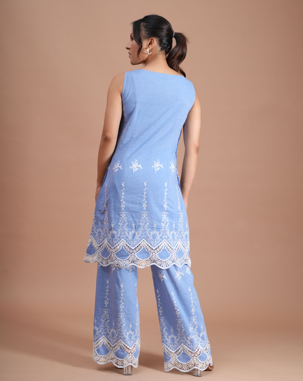 Woman wearing a light blue embroidered outfit on a beige background