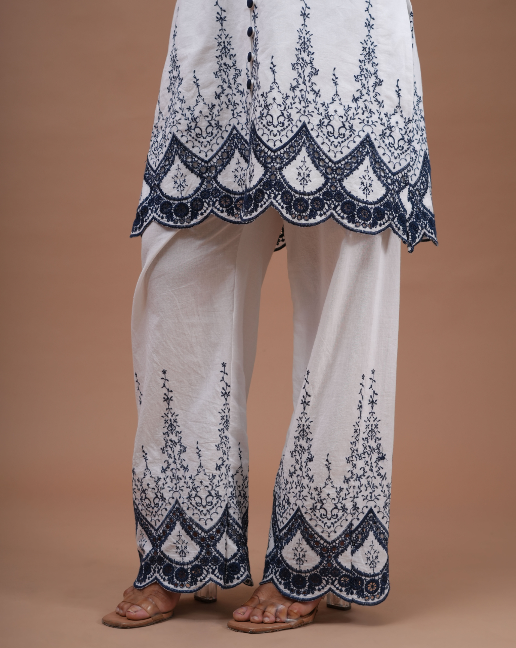 White outfit with blue floral embroidery on a beige background