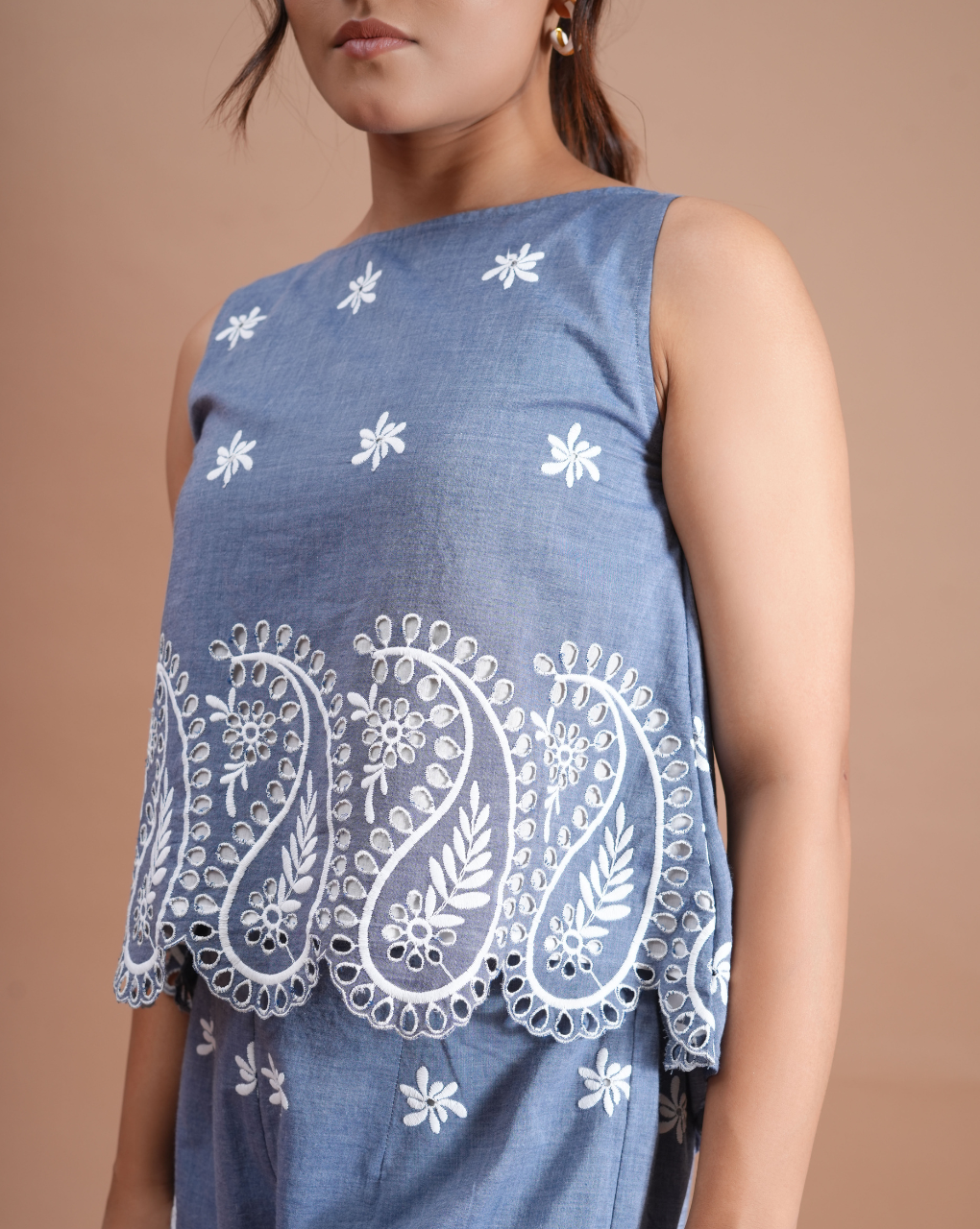 Blue sleeveless top with white floral embroidery on a beige background
